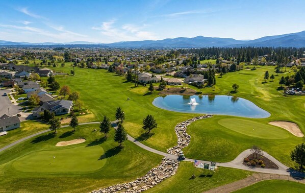 A golf course with a pond, houses, and mountains in the background.
