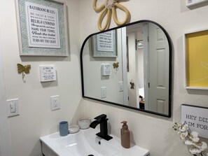 Un baño con lavamanos, espejo y varios carteles con indicaciones.