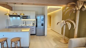 A modern kitchen with a central island, built-in appliances, and a dining area with wicker stools. - MŪTE Collection at Spirit of Terrenas (Las Terrenas)