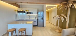 Una cocina moderna con una isla central, electrodomésticos integrados y una zona de comedor con taburetes de mimbre.