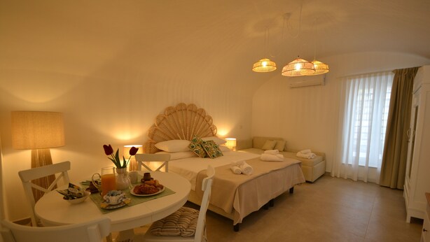 A hotel room with a dining table, chairs, a bed with a canopy, a bedside table with a lamp, and a window with curtains. - Petra Lavea (Pompei)