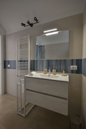 A modern bathroom with a white vanity, a towel rack, a mirror, and a light fixture. - Petra Lavea (Pompei)