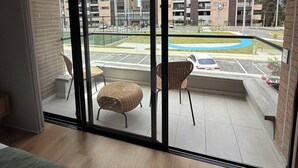 Un balcon avec des fauteuils en osier, une vue sur un immeuble à plusieurs étages et un espace de stationnement.