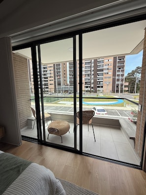 Un balcón con sillas de mimbre, vista a un edificio de varios pisos y un estacionamiento.