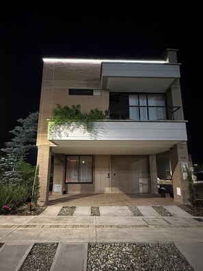 Un edificio moderno a due piani con tetto piatto, ampie finestre e un balcone con piante.