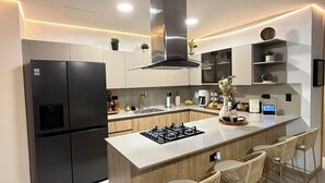 Une cuisine moderne dotée d’un îlot central, de tabourets de bar, d’un réfrigérateur encastré et d’une cuisinière.
