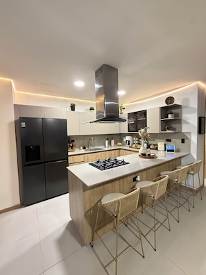 Una cocina moderna con una isla central, taburetes de bar, nevera empotrada y estufa.