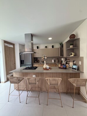 Una cucina moderna con isola centrale, sgabelli da bar, piano cottura integrato e una cappa aspirante di grandi dimensioni.