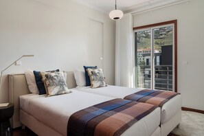 Ein Hotelzimmer mit zwei Betten, einem Nachttisch, einer Lampe und Blick durch eine Schiebetür.