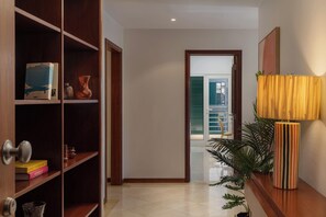 Ein Flur mit einer Holztür, einem Regal mit Büchern und einer Vase, einer Topfpflanze und einer Lampe.