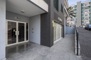 Ein modernes Gebäude mit Glastür, einem Schild mit der Aufschrift 'AÚNCA' und einem Parkplatz mit Autos.