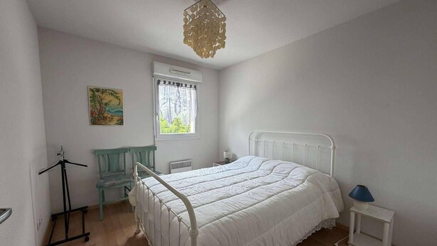 Quarto com cama, janela, cadeira, mesinha e luminária pendente.