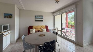 Uma sala de jantar com uma mesa redonda, cadeiras, um sofá, uma televisão e uma varanda com mobiliário para exterior.