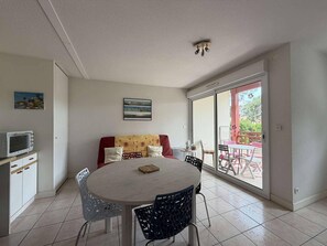 Ein Essbereich mit einem runden Tisch, Stühlen, einer Couch, einem Fernseher und einem Balkon mit Gartenmöbeln.
