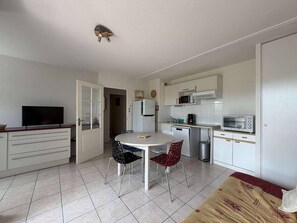 Eine kompakte Küche mit Mikrowelle, Toaster und Kühlschrank. Ein Esstisch mit zwei Stühlen und ein Fernseher auf einem Schrank.