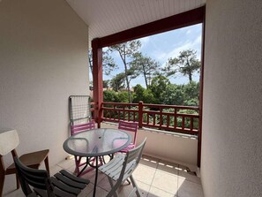 Ein Balkon mit Glastisch und Stühlen, einem roten Geländer und Blick auf Bäume.