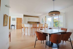 Eine moderne Küche mit weißen Schränken, ein Essbereich mit Holzsesseln und ein großes Fenster, das für natürliches Licht sorgt.