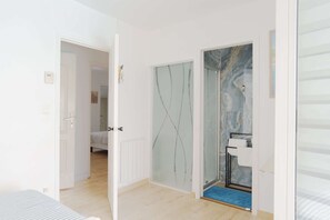 Ein Zimmer mit einem Bett, einer Glasdusche und einer Tür zu einem weiteren Raum.