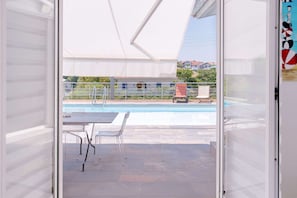 An open sliding door to a balcony with a pool, outdoor furniture, and a view of houses in the background. - A very beautiful house with a pool (ST JEAN DE LUZ)