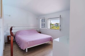 A bedroom with a bed, a nightstand, a lamp, a window with a view, and a door. - A very beautiful house with a pool (ST JEAN DE LUZ)