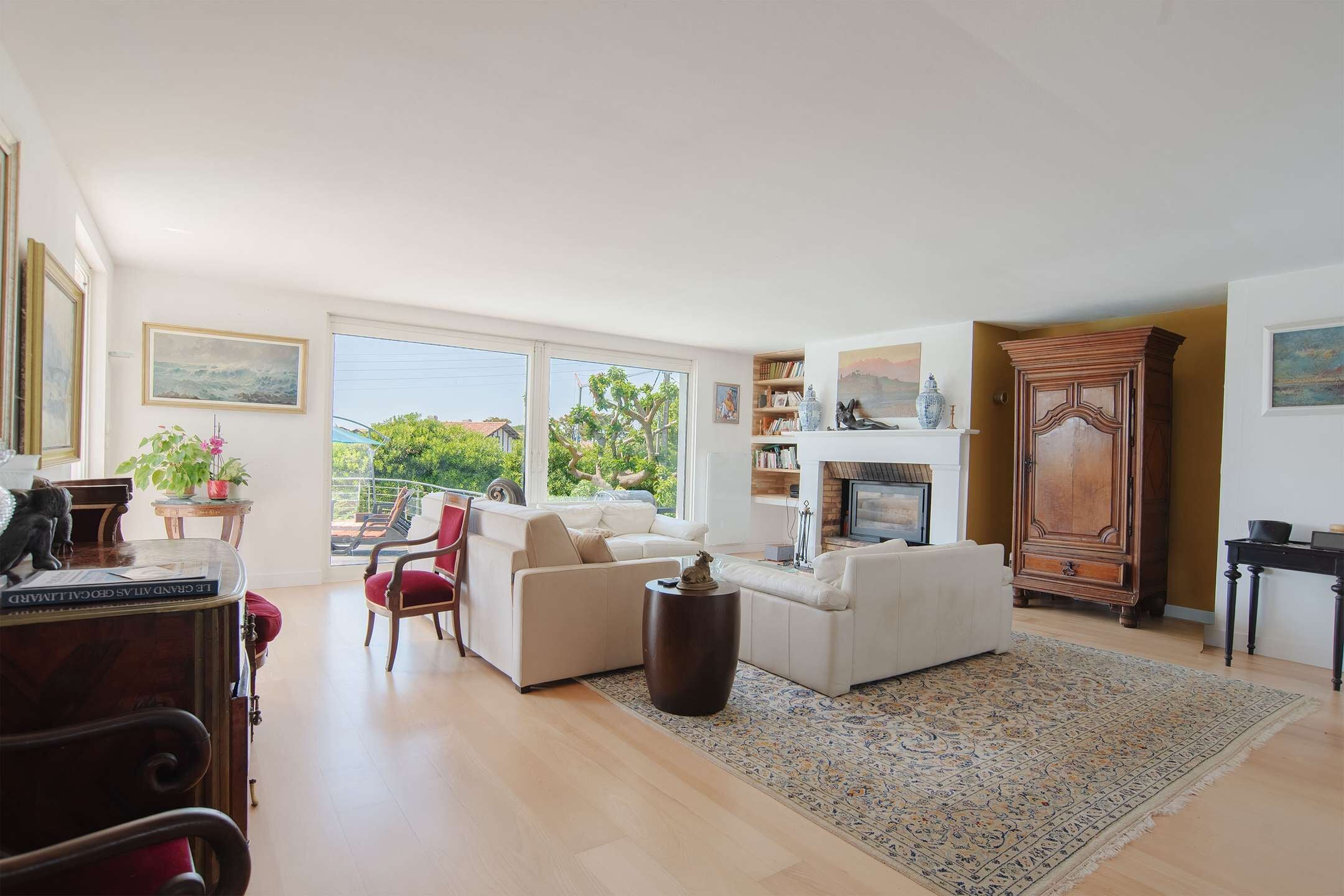 A spacious living room with a fireplace, a large window, and a view of greenery outside.