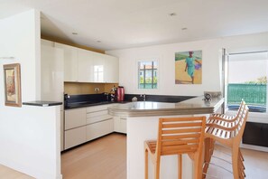 A modern kitchen with white cabinets, a black countertop, and wooden chairs. - A very beautiful house with a pool (ST JEAN DE LUZ)