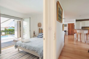Ein Schlafzimmer mit Bett, Blick auf den Swimmingpool und einer Küchenzeile mit Holzkreislern.