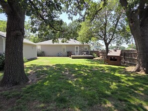 A backyard with a lawn, a wooden playhouse, and a house with a covered patio.