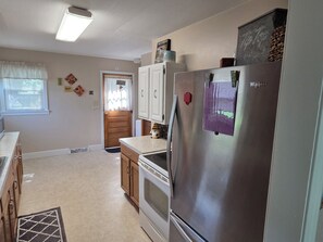A kitchen with a stainless steel refrigerator, wooden cabinets, a built-in oven, and a window with blinds.