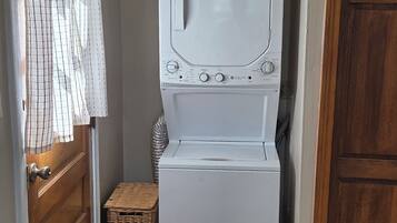 Pesuhuone, jossa on etuaukollinen pesukone ja kuivausrumpu, rottinkikori ja raidallinen verho, joka on oven edessä.