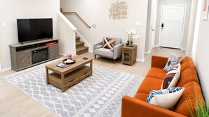 A modern living room with a TV, sofa, coffee table, and staircase. - [GS] 3BR+3BR I 2 Kitchens I Two Adjacent Townhomes I Brand New & Family-Friendly (San Antonio)