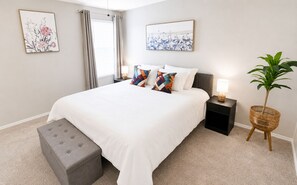 A bedroom with a bed, a nightstand, a lamp, a plant, and artwork on the walls. - [GS] 6BR + Parking I Two Adjacent Townhomes I Fully Stocked & Family-Friendly (San Antonio)