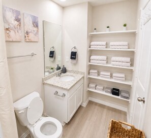 A modern bathroom with a toilet, sink, and shelves for towels. - [GS] 6BR + Parking I Two Adjacent Townhomes I Fully Stocked & Family-Friendly (San Antonio)