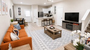 A modern living room with a sofa, coffee table, and TV. - [GS] 3BR+3BR I 2 Kitchens I Two Adjacent Townhomes I Brand New & Family-Friendly (San Antonio)