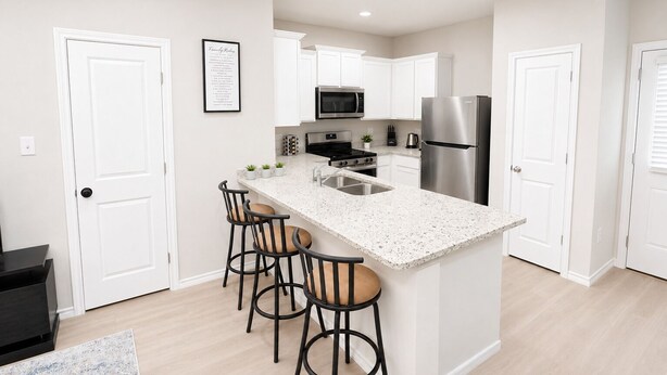 A modern kitchen with white cabinetry, a stainless steel refrigerator, a microwave, and a gas stove. There are three bar stools with cushioned seats. - [GS] 3BR+3BR I 2 Kitchens I Two Adjacent Townhomes I Brand New & Family-Friendly (San Antonio)