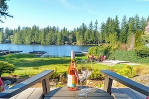 Ein Tisch mit einer Weinflasche und Gläsern, mit Blick auf einen See und Wald.