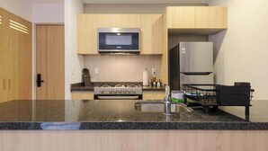 A modern kitchen with wooden cabinets, a stainless steel microwave, a built-in oven, a refrigerator, and a granite countertop. - w* | Upscale Loft w/ Balcony in Roma Norte (Ciudad de México)