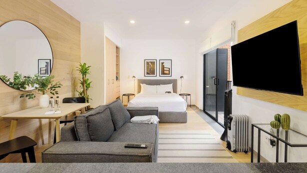 A modern hotel room with a bed, a sofa, a TV, a desk, and a small table with plants. - w* | Upscale Loft w/ Balcony in Roma Norte (Ciudad de México)