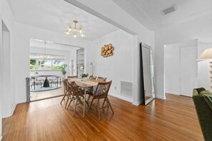 Un vaste espace dédié à la salle à manger, avec une table et des chaises en bois, un lustre et un grand miroir.