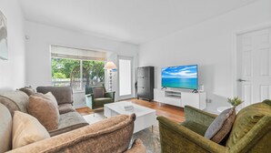 Ein modernes Wohnzimmer mit Sofa, Sesseln, Couchtisch, Fernseher und Blick ins Freie.