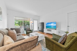 Un salon moderne avec un canapé, des fauteuils, une table basse, un téléviseur et une vue sur l’extérieur.
