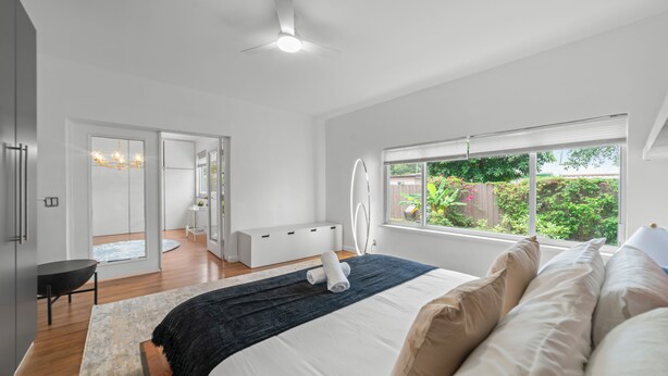 Ein Schlafzimmer mit Bett, Schreibtisch, Stuhl, Fenster mit Blick ins Grüne und Deckenventilator.