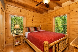 Une chambre dans une cabane en bois, avec un lit, une table de chevet, une lampe et de grandes fenêtres.