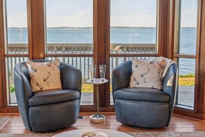 Zwei Ledersessel mit passenden Kissen, ein kleiner runder Tisch mit einem Glas und Blick auf das Wasser durch große Fenster.