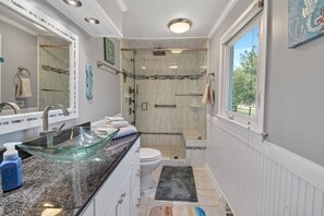 Un baño con lavamanos de vidrio, ducha, inodoro y ventana.