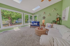 Una habitación amplia con un gran ventanal, un sofá blanco, un sillón azul y una mesita con una lámpara.