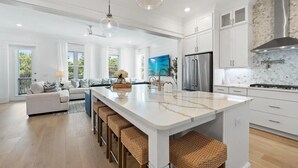 Una cocina moderna con armarios blancos, una isla grande, electrodomésticos de acero inoxidable y vistas al exterior.