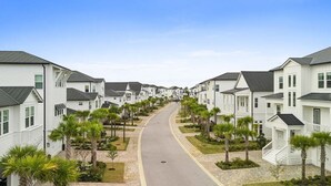 Una calle residencial con casas blancas, una carretera curva y palmeras.