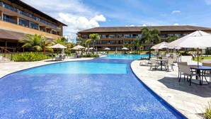 A hotel with a large swimming pool, outdoor seating, and a building with multiple floors. - Eco Resort Apartment - Carneiros Beach (Tamandaré)