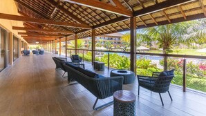 A covered outdoor area with seating, a pool, and a view of a resort. - Eco Resort Apartment - Carneiros Beach (Tamandaré)